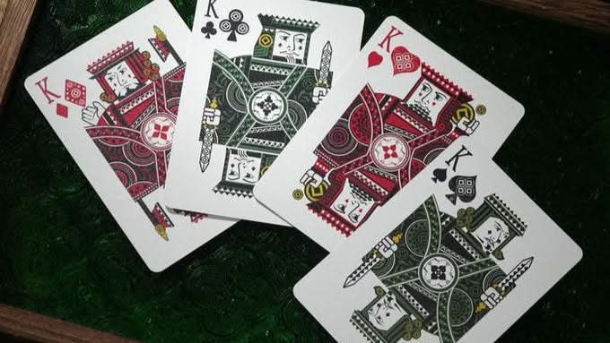 Four playing cards from the n2g coipix deck featuring kings from different suits on a green surface.