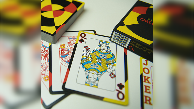 Close-up of Chris Cards Covered Circle (Standard Edition) Playing Cards featuring the Queen of Clubs and Joker cards, with the box and deck displaying bold geometric designs in red, yellow, and black in the background.