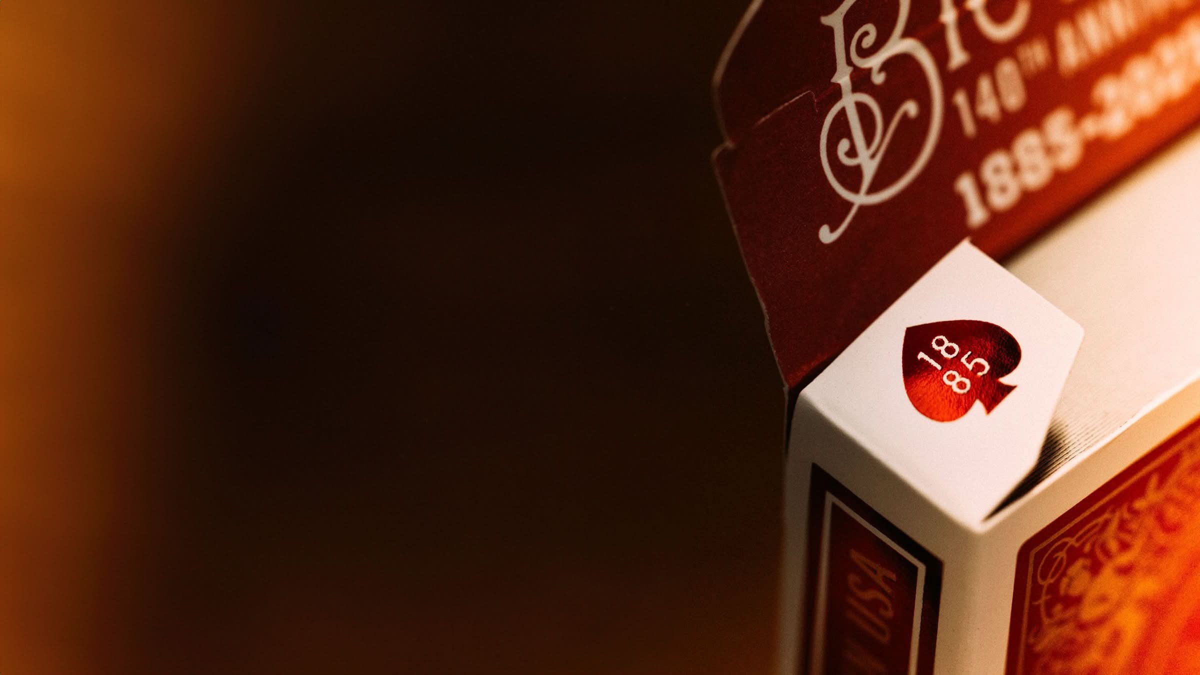 Close-up of a Bicycle 140th Anniversary playing card tuck box flaps with 1885 luxurious red foil detailing on a deep red background. Available at 52Kards for collectors, magicians, and card enthusiasts.