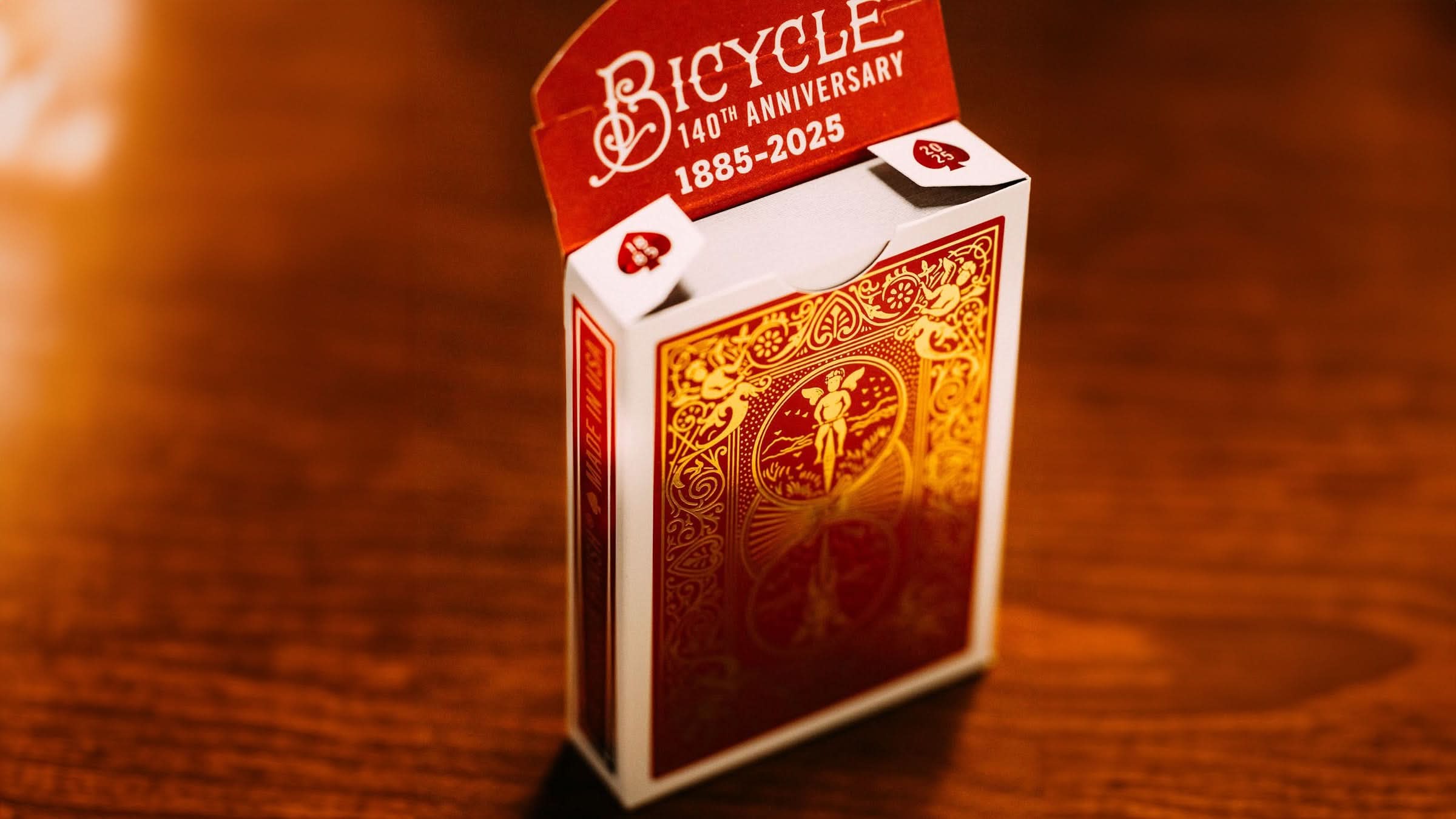 full wide shot of Bicycle 140th Anniversary playing tuck box back with luxurious gold foil detailing on a deep red wooden background. Available at 52Kards for collectors, magicians, and card enthusiasts.