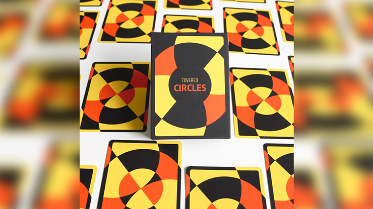 Chris Cards Covered Circle (Standard Edition) Playing Cards box surrounded by multiple card backs laid out in a grid pattern. The bold geometric designs in red, yellow, and black create a visually striking arrangement.