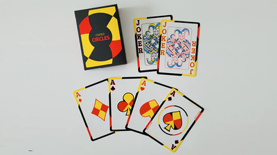 Chris Cards Covered Circle (Standard Edition) Playing Cards featuring bold geometric designs in red, yellow, and black, with custom artwork. The deck box displays the title 'Covered Circles,' and the cards showcase Jokers and all four Aces with modern and vibrant patterns.