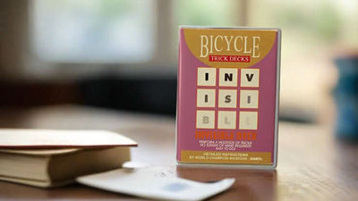 Purple packaging around the Bicycle Invisible Deck tuck box on a tabletop with cards and books in the background