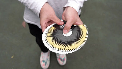 Hands displaying a circular thumb fan of black, white and yellow Cardistry Fanning cards